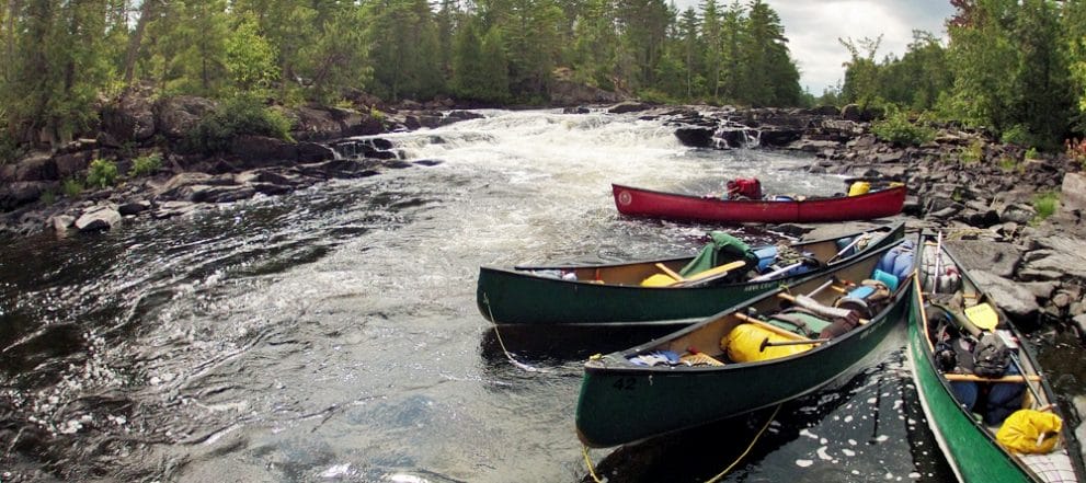 Canoes tied to shore with whitewater in background HEADER