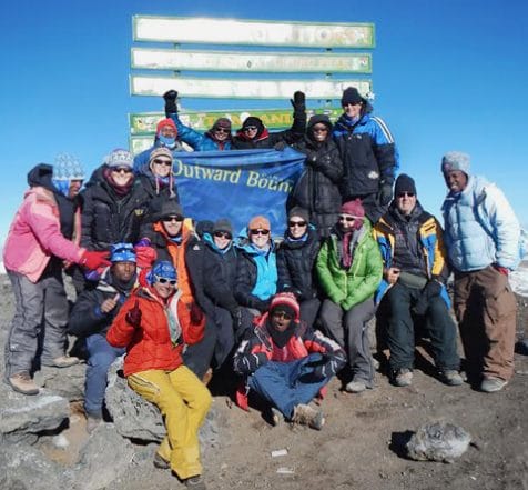 Group of climbers at the top of Mount Kilimanjaro holding an Outward Bound Canada flag