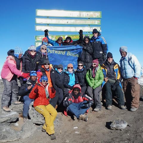 Group of climbers at the top of Mount Kilimanjaro holding an Outward Bound Canada flag