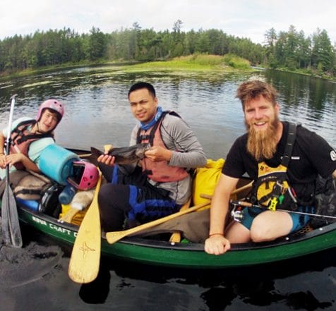 Three male particpants in canoe one holding a fish