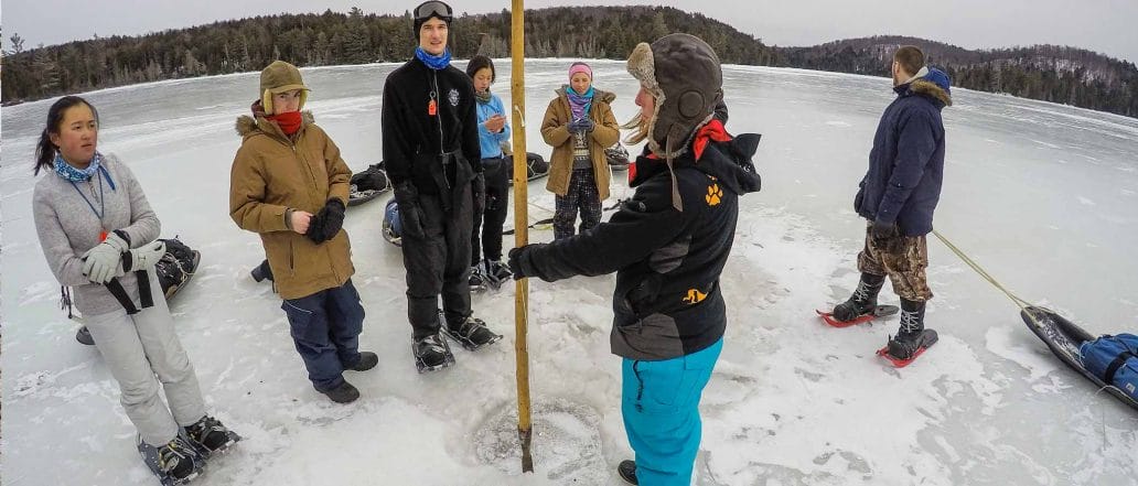 Image of an instructor teaching a group of youth how to measure the depth of the ice on a frozen lake