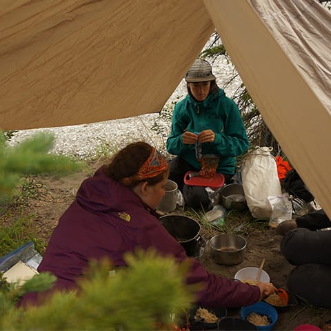 two women preparing food under a tarp