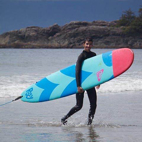 teen carrying a surfboard on a beach