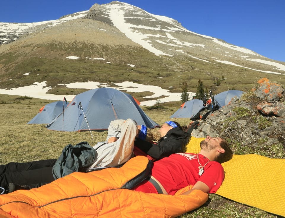campers in sleeping bags with rocky mountains in background