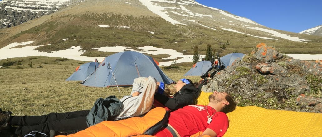 campers in sleeping bags with rocky mountains in background