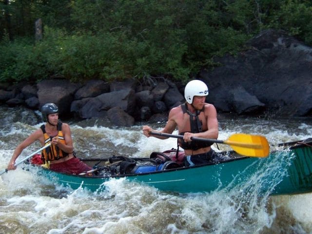 two boys paddling a canoeing in white water rapids