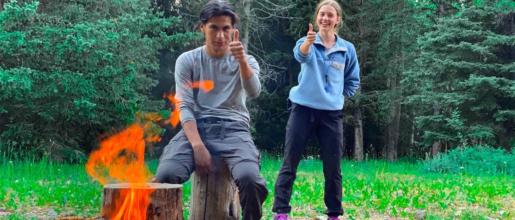 Image of 2 people putting their thumbs up around a fire
