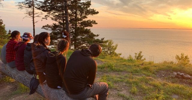 group of seven students watching sunset over ocean