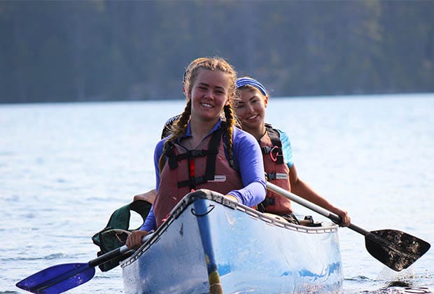 Image of two teens paddling blue canoe