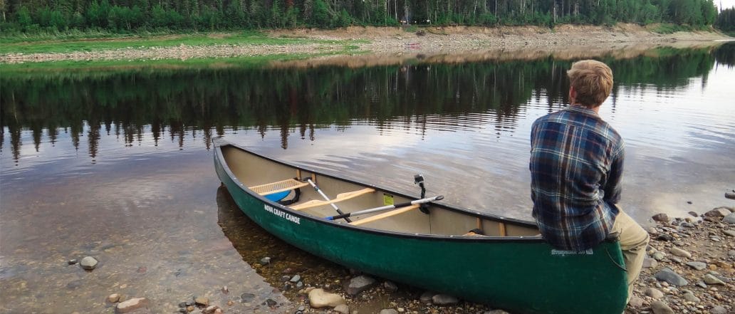 Image of the back of teen sitting on a canoe parked on the bank