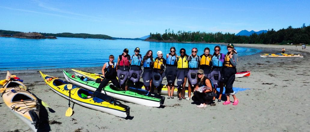 Image of a group of kayakers standing and sitting on the shore