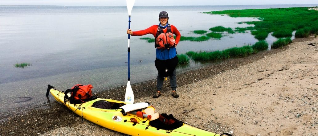 Image of a kayaker standing next to their kayak with a paddle