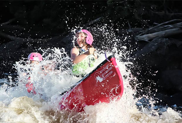 Image of water splashing on two teen sitting in a canoe