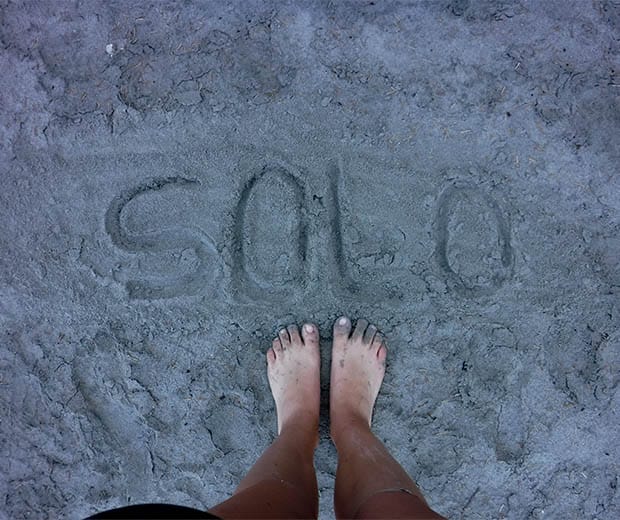 Image of someone standing in front of the word solo written in the sand