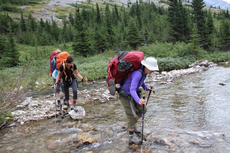 Three backpackers crossing a stream