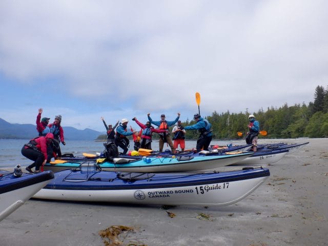 Image of group of people surrounding beached kayaks
