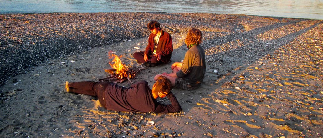 Image of three teens sitting and lying near a fire