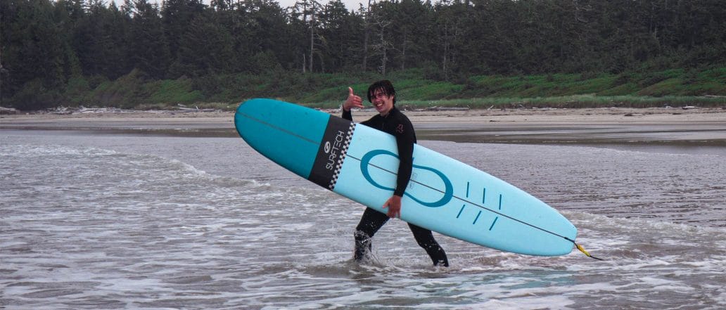 Image of a teen walking through the water with their surfboard