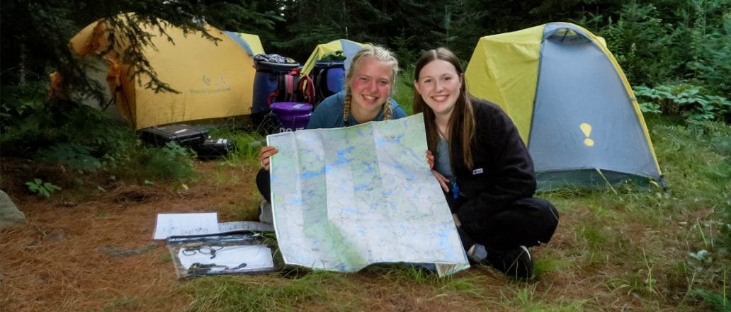 Image of two teens showing a paper map sitting in front of tents