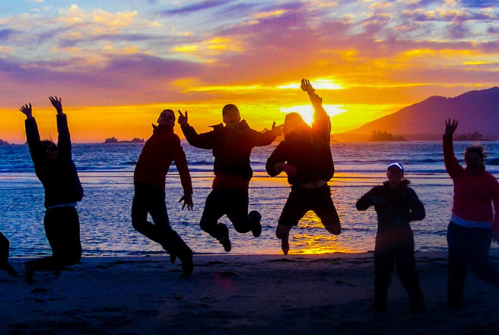 Image of a group, jumping at seashore at dusk