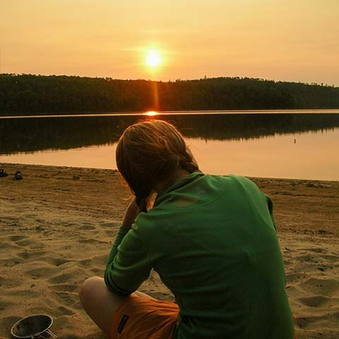 Image of a person sitting on a beach looking at the sunset