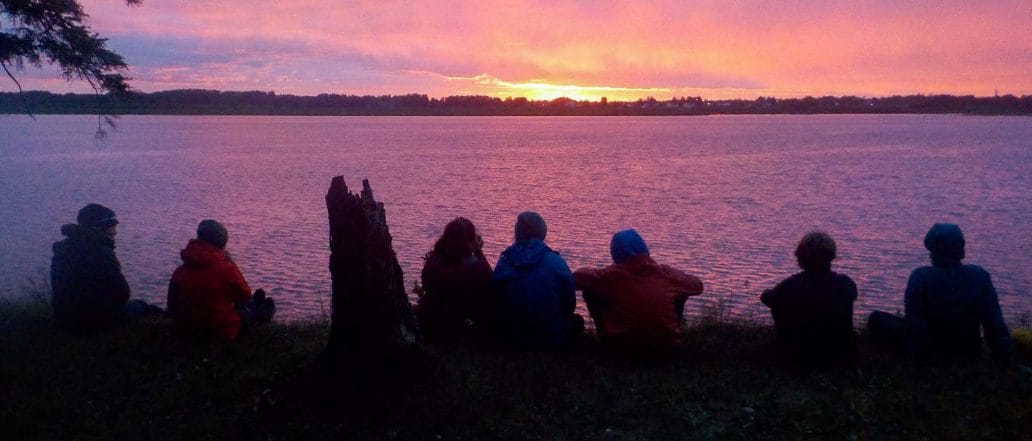 Image of a gorup of people watch the sunset over a lake