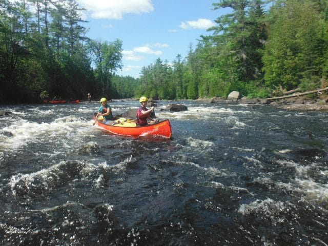 Two people in a red canoe paddling through rapids.