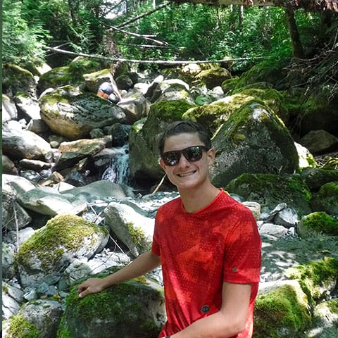 Image of a teen in sunglasses in front of a rocky stream