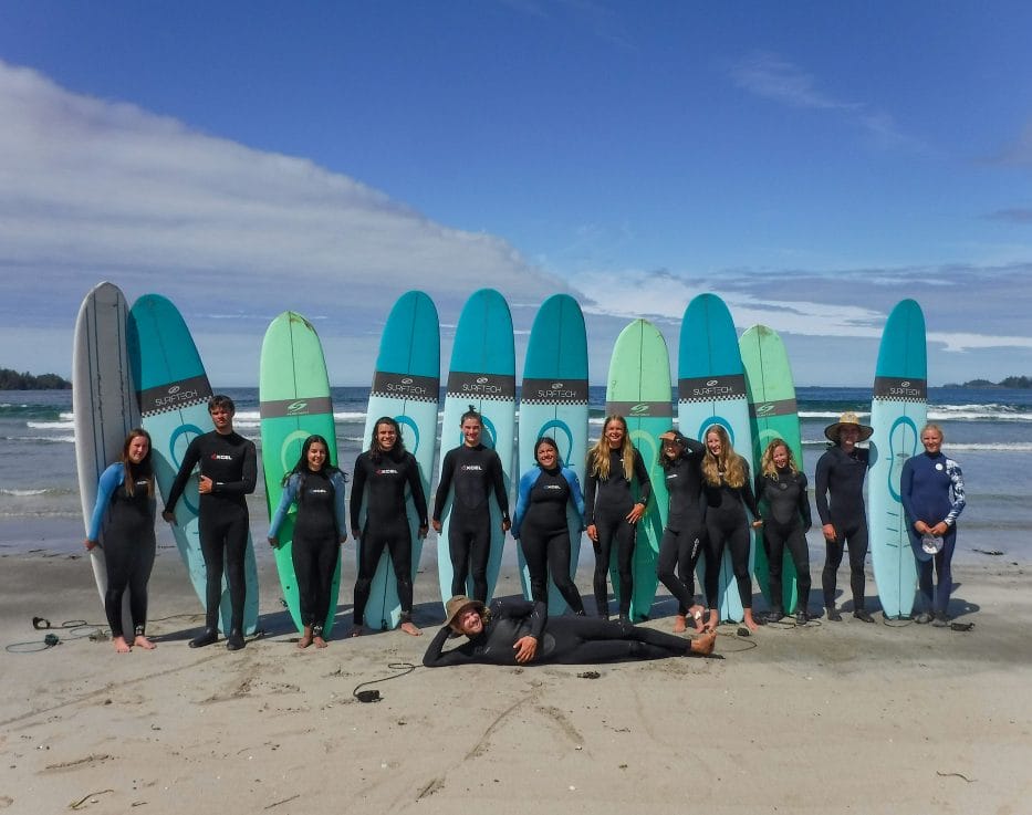 Image of a line of teens standing in front of upright surfboards