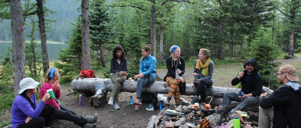 Group of people sitting on logs around a firepit