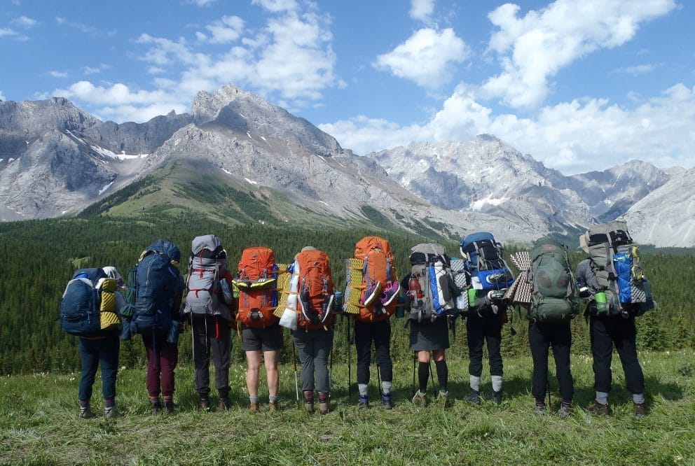 Ten people with hiking backpacks looking out at Mountains