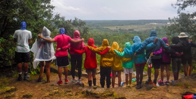 Group of people linked arms in rainbow-coloured rain jackets