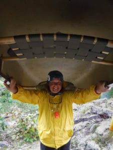 Person in a yellow rain coat carrying a canoe over their head