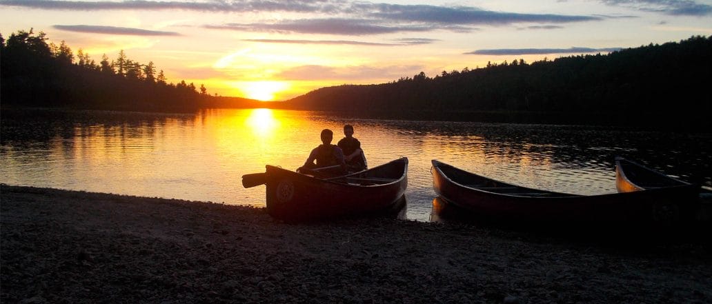 Image of two people sitting in canoe at the bank at sunset