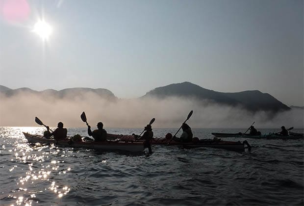 Image of a group of people kayaking in the foggy sea on a beautiful morning