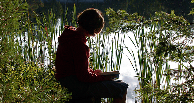 Image of a teen journaling next to tall grass