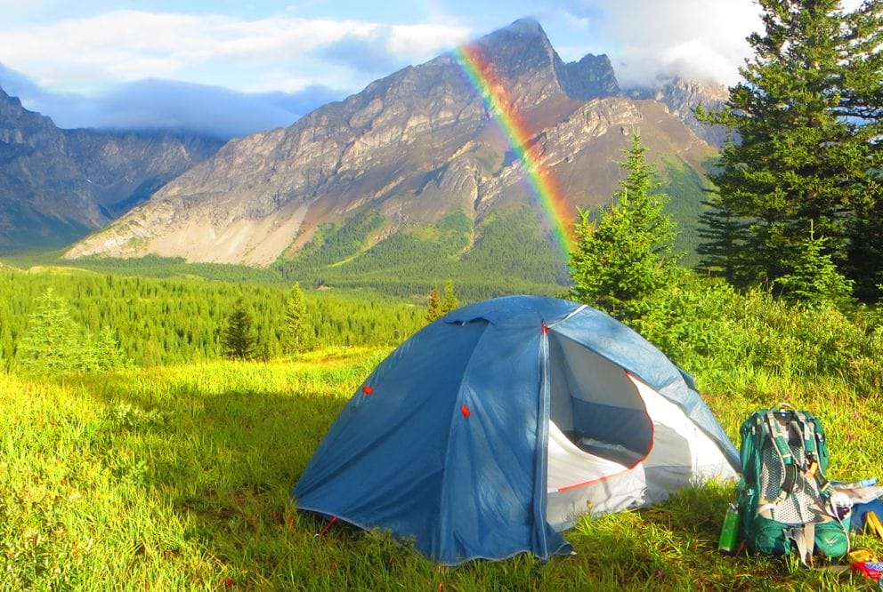 Image of a tent with breathtaking view of rainbow and mountains behind