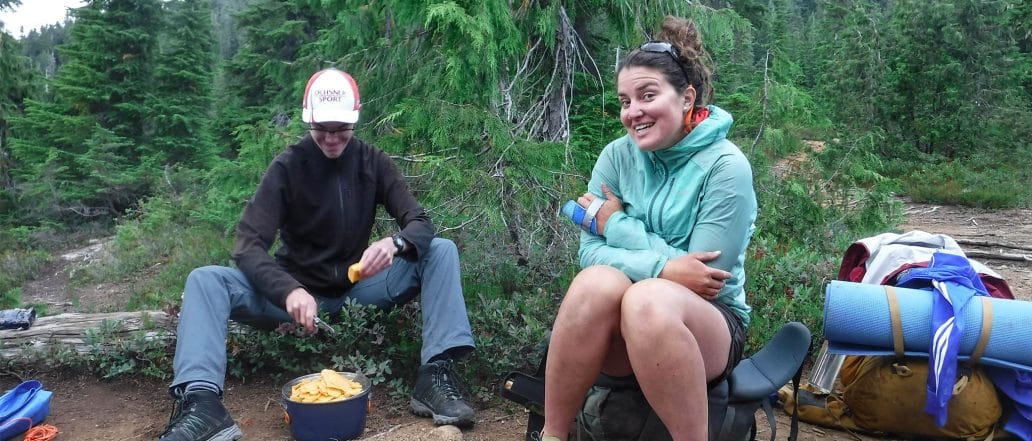 Image of 2 people sitting on a log while cooking