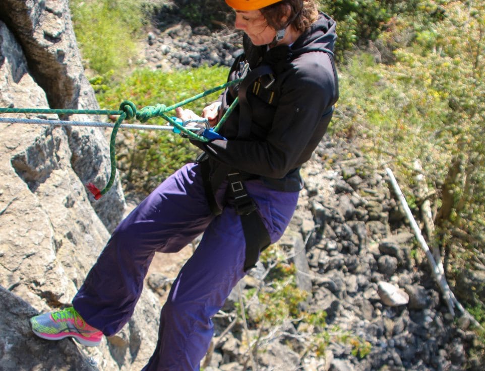 Image of a person in a harness and helmet leaning off a rock