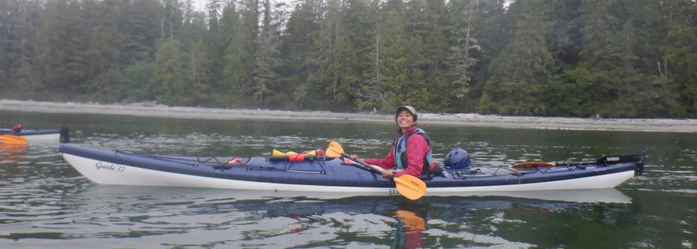 Young BIPOC female outdoor guide Shams Ben Temessek paddles a kayak in a lake