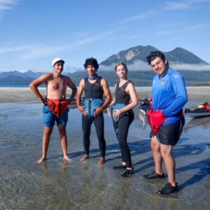 four teens smiling in wet suits with lake and mountain range behind