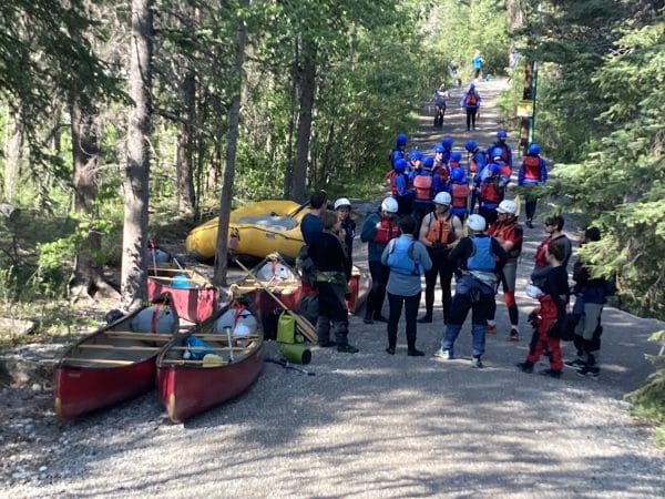 group of OBC staff in white water canoeing gear, waiting by a boat in the forest