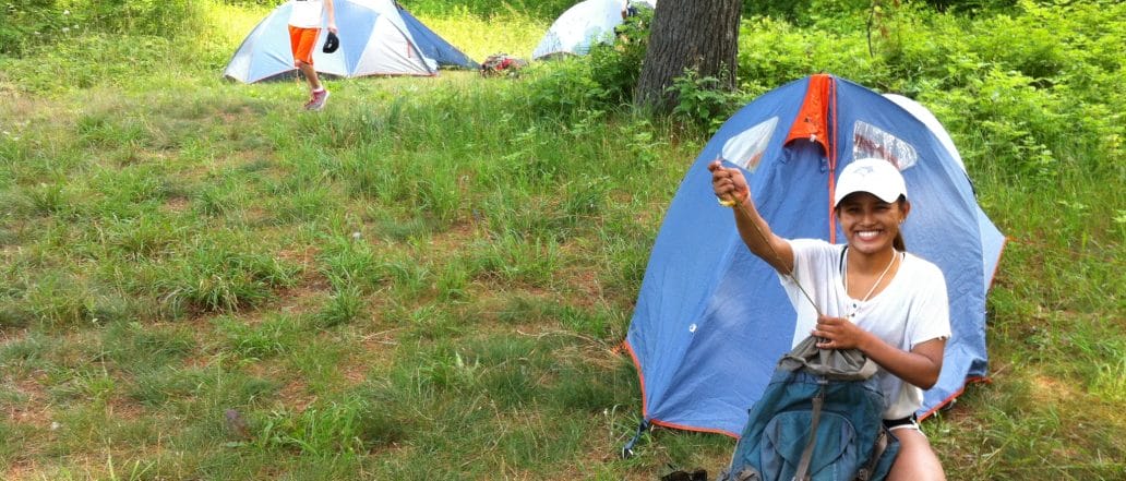 girl pitching a tent smiling with grass behind her