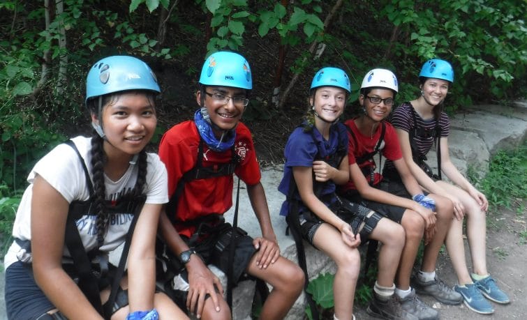 group of teens smiling sitting near high ropes course