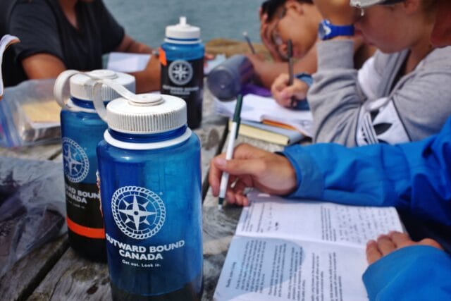 photo of obc participants writing in journals next to obc logo water bottles