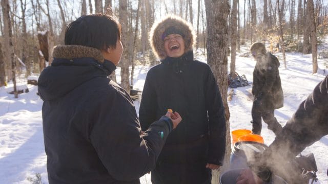a teen in a parka laughing with fellow teen with snowy background
