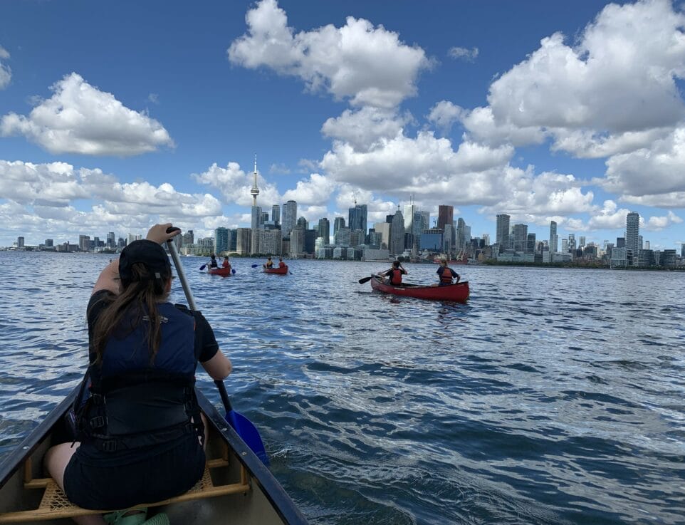 group of teens canoeing toronto islands with skyline in forefront
