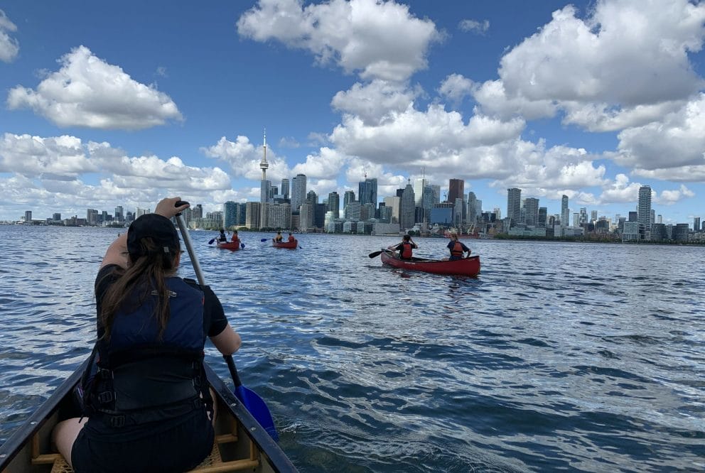 group of teens canoeing toronto islands with skyline in forefront