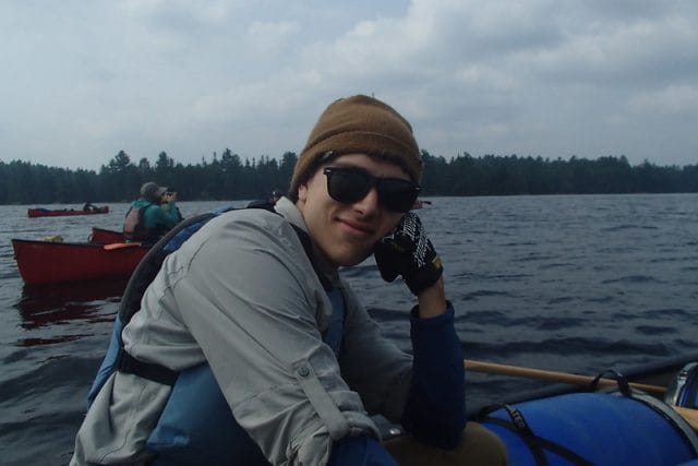 teen smiling at the camera while sitting in a canoe on a lake