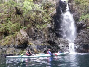 Image of 2 people in a kayak paddling near a waterfall